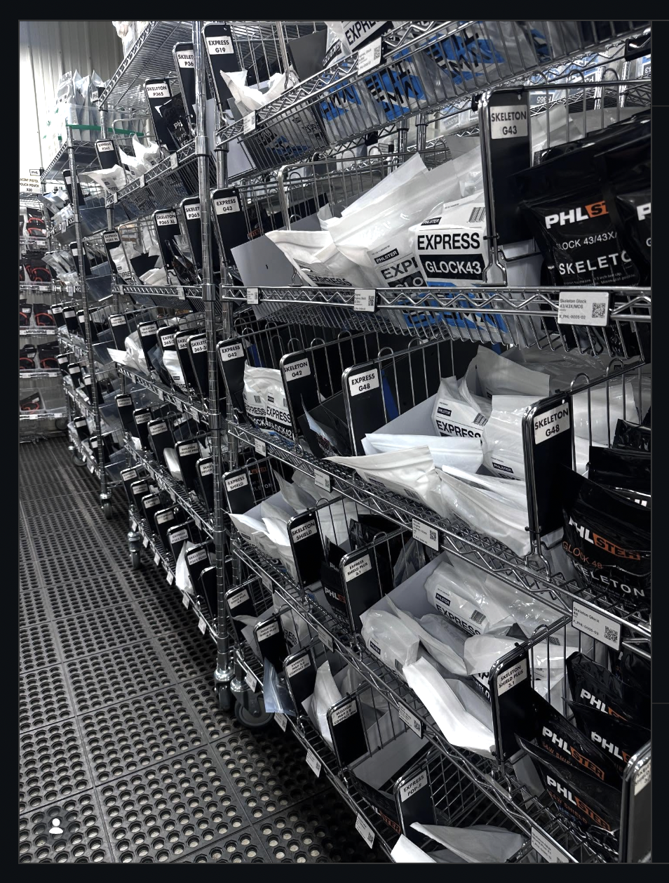 PHLster's in-house fulfillment shelves stocked with Express and Skeleton holsters labeled by gun model — the operation built and staffed in-house instead of outsourced to an Amazon warehouse